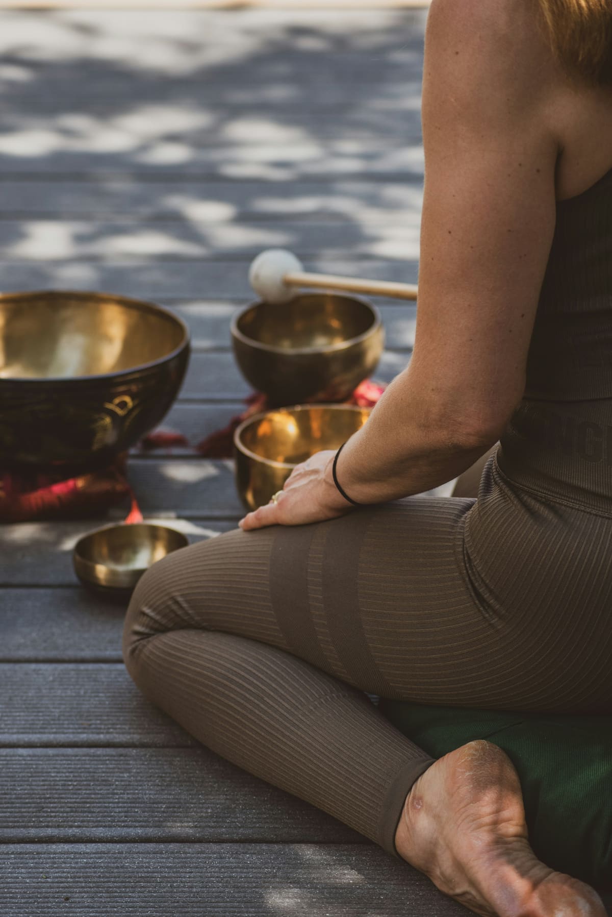 Bols tibétains en cuivre disposés sur une terrasse en bois, à côté d'une prof en posture du lotus