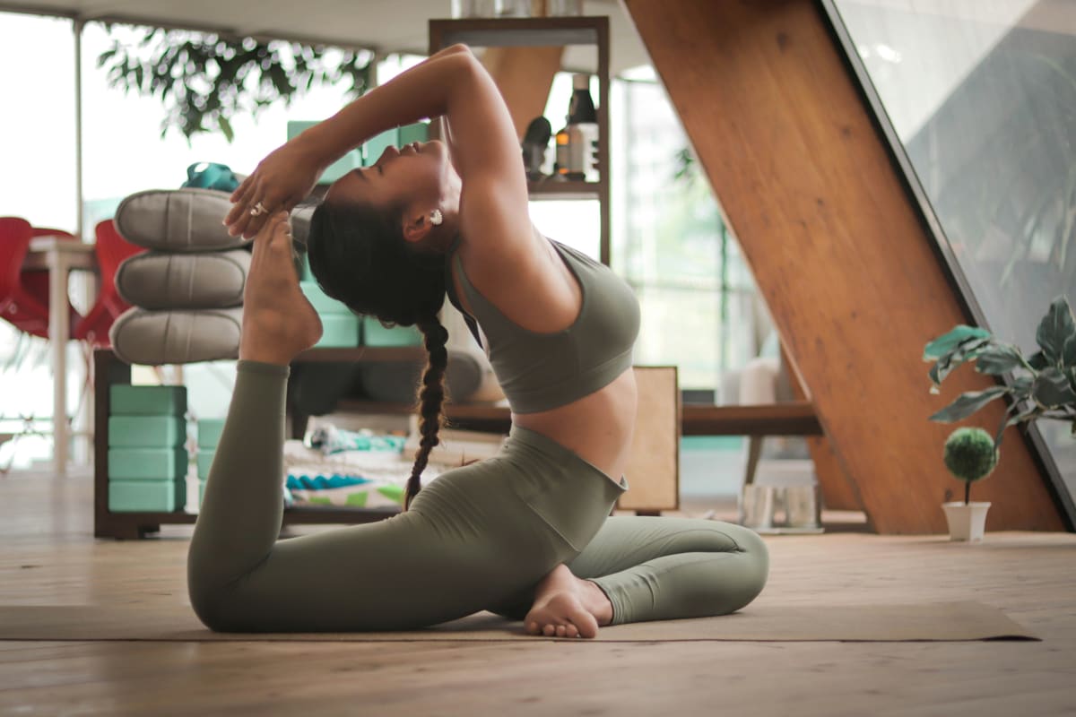 Prof de yoga dans une posture du pigeon dans un studio intérieur design avec mobilier en bois clair