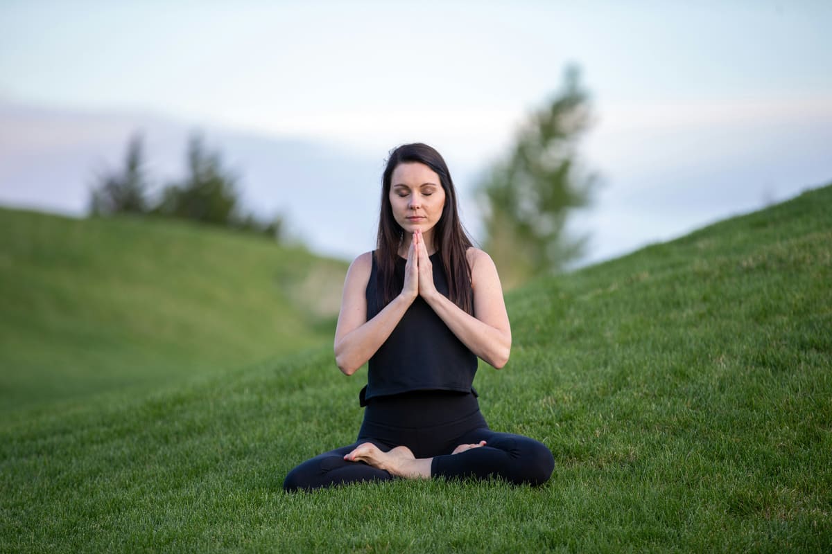 Femme en posture de méditation namasté assise dans l'herbe au coucher du soleil